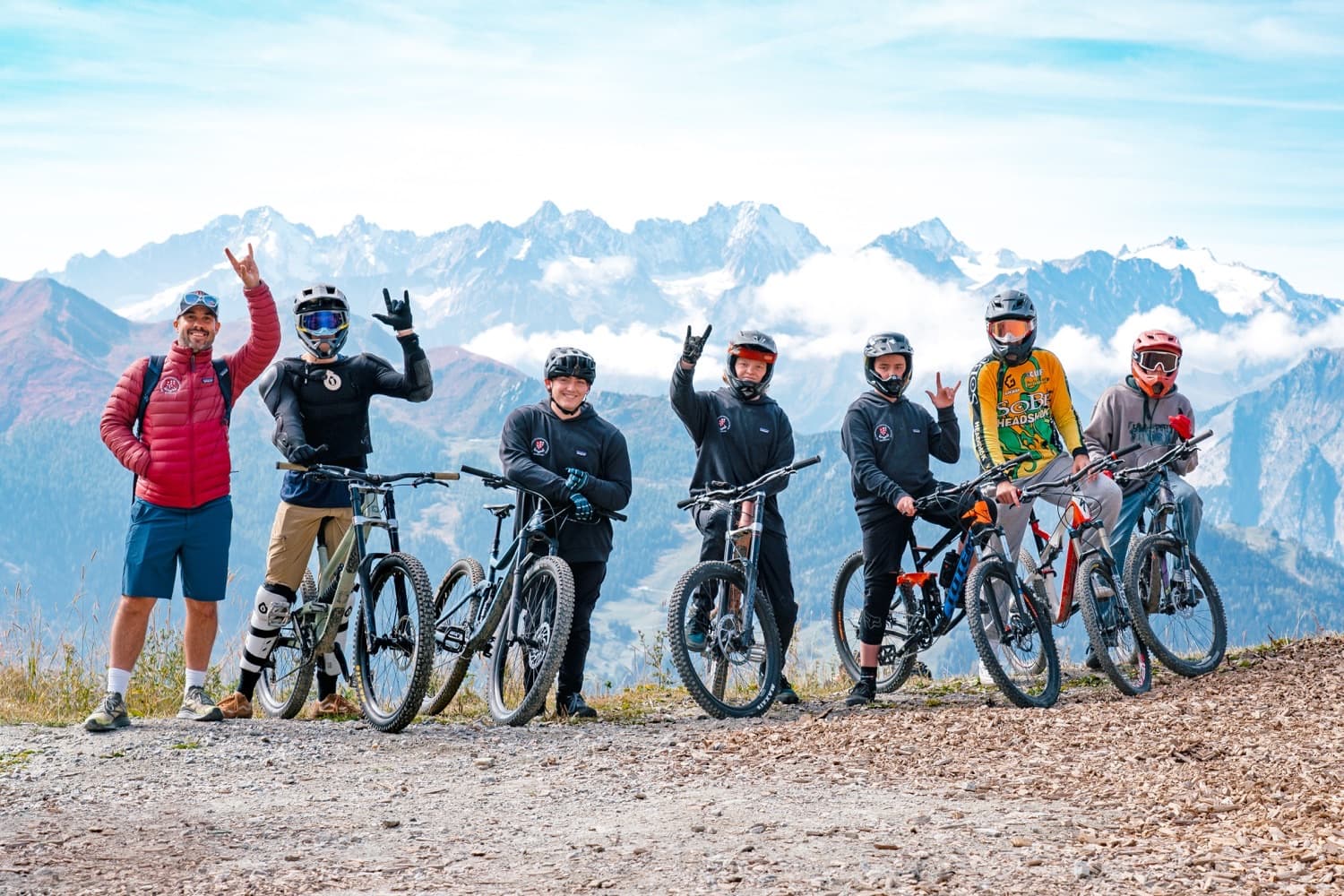 アルプスの山頂でマウンテンバイクと共に並ぶ生徒たちとコーチの写真